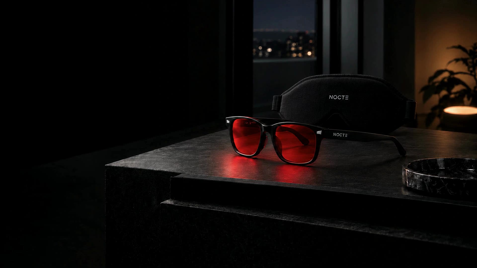 Lentes NOCTE rojos y antifaz negro sobre piedra oscura, con una ventana nocturna al fondo.